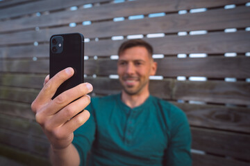 Young happy attractive man using smartphone outdoors at sunset. Man holding modern black mobile phone. Man having a facetime video call. Looking at smartphone 