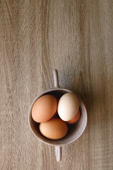 Ceramic bowl filled with fresh free range eggs on wooden table. Flat lay.