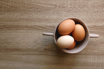 Ceramic bowl filled with fresh free range eggs on wooden table. Flat lay.