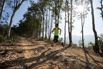 Obraz premium Fitness woman trail runner running on sunrise tropical forest mountain peak
