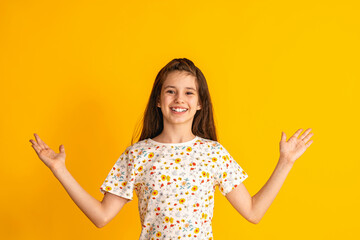 cheerful girl about 10 years old in a colorful T-shirt spreads her arms to the sides and a happy smile on a yellow background. A happy child enjoys success and victory. Discounts and sales