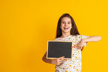 cheerful, happy teenage girl points her finger at an empty blackboard, copying the space for the text. smiling, enthusiastic teenager in bright T-shirt is showing off. Advertising concept. Copy space