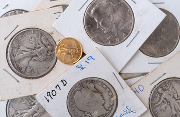 Old coin collection in protective wrappers with a gold liberty coin loose on top.