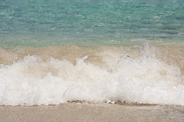 a small wave breaking at the beach, turquoise water