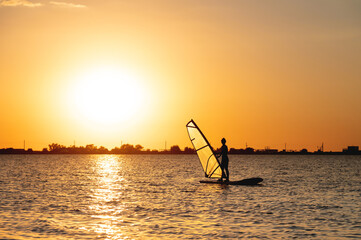 Woman windsurfer silhouette at lake sunset. Beautiful beach landscape. Summer water sports activities, recreation and travel concept