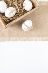 The concept of Easter. White chicken eggs in a wooden basket on hay against a white table background. Copy space. Flat lay.