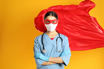 Doctor dressed as superhero posing on yellow background. Concept of medical workers fighting with...