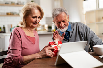 Senior couple having video call. Happy husband giving his wife a gift.