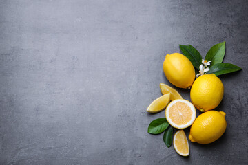 Many fresh ripe lemons with green leaves and flowers on grey table, flat lay. Space for text