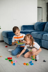 Two young children boy and girl sit on the wooden floor of the house playing educational games