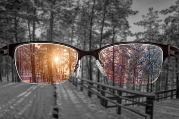 Colorful view of sunset in winter forest focused in women's glasses and monochrome background. View...