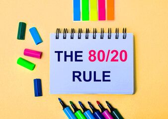 On a beige background, a notebook with the words THE 80 20 RULE, bright felt-tip pens and stickers