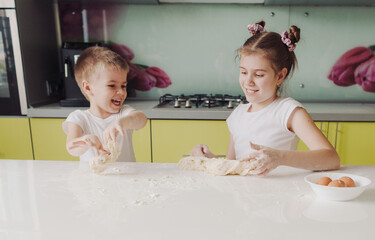 beautiful young brother and sister messing around with dough in the kitchen while cooking. young...