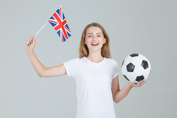 Young woman with Great Britain flag and a soccer ball in her hands, looking straight into the camera, isolated on gray background. British women's football.