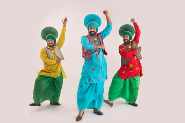 Three Bhangra dancers performing a dance step with hand gestures.	