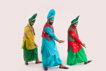 Three Bhangra dancers performing a dance step with hand gestures.	
