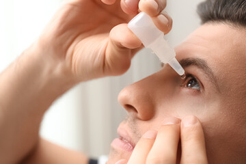 Man using eye drops on blurred background, closeup