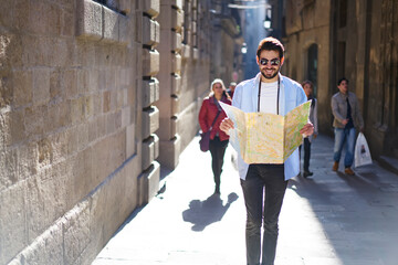 Positive ethnic man walking on street with paper map