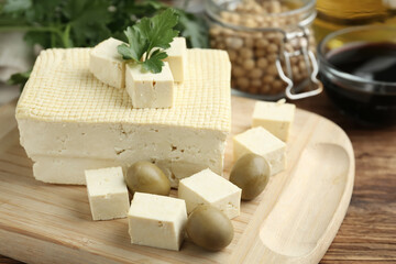 Cut tofu with olives and soya beans on wooden table, closeup