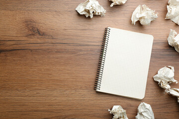 Notebook and crumpled sheets of paper on wooden background, flat lay. Space for text