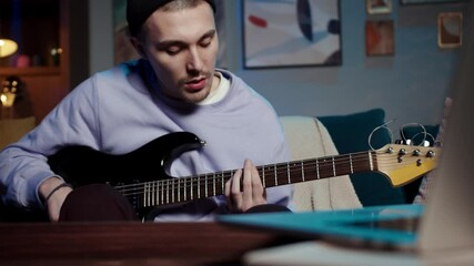 young man with guitar playing songs in the room at home. Online guitar lessons concept. Male guitarist practicing chord grips. Remote learning during coronavirus lockdown