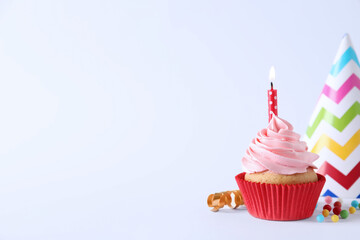 Delicious birthday cupcake with burning candle, sprinkles and party decor on white background,...
