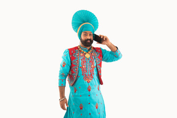 A man in Bhangra Costume talking over phone.	