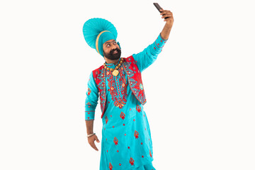A man in Bhangra Costume taking a selfie in his phone.	