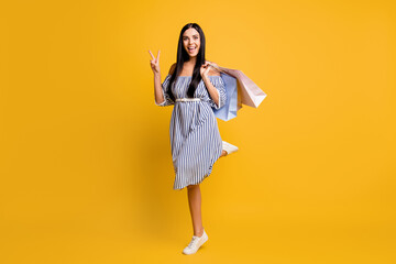 Full length photo of charming woman dressed off-shoulders dress holding bags showing v-sign...