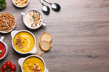 Different tasty cream soups and bread on wooden table, flat lay. Space for text