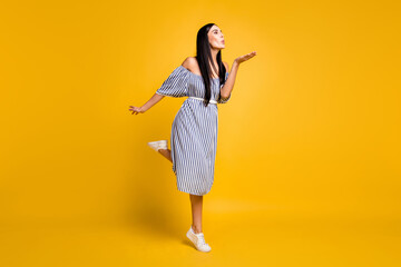 Fototapeta na wymiar Full length photo of charming sweet young lady wear striped dress sending kiss arm empty space isolated yellow color background