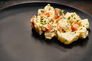 Black plate with Russian salad of potatoes, carrots, peas, egg and mayonnaise. Food concept.