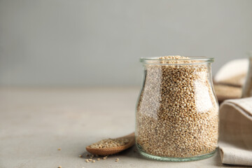 Jar and wooden spoon with white quinoa on light grey table. Space for text
