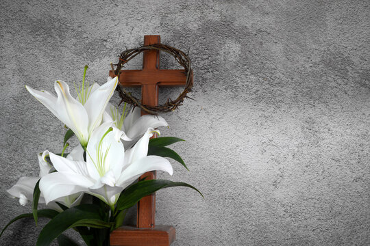 Cross with white lilies and crown of thorns on grey background. Christianity Easter concept.