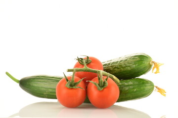Several green cucumbers and red ripe, cocktail tomatoes on a twig, close-up, isolated on white.