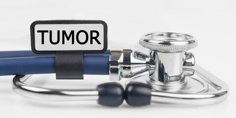 On the white surface lies a stethoscope with a plate with the inscription - TUMOR