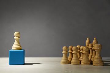 White chess piece standing out from others on wooden table against grey background