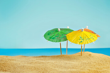 Beach umbrellas on the sand. Stylized cardboard beach. Paper umbrellas for cocktails in the background. The concept of rest, sea and vacation.