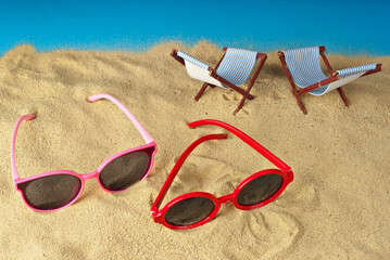 Fototapeta na wymiar Pink glasses on the sand close up. Glasses on a beach chair background. Beach chairs on a background of blue water. Summer, sea and vacation concept.
