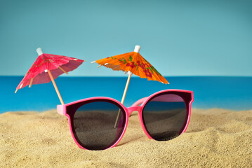Pink glasses on the sand close up. Glasses on the beach on a background of paper umbrellas for cocktails. Summer, sea and vacation concept.