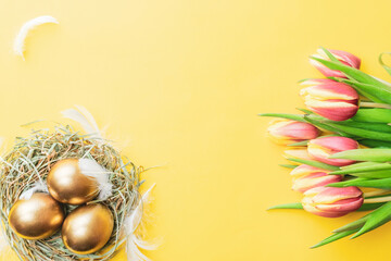 Naklejka na ściany i meble Easter Golden colour eggs in basket with spring tulips, white feathers on pastel yellow background in Happy Easter decoration. Festive decoration in flat lay.