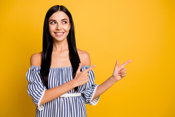 Photo of pretty shiny young lady wear striped dress pointing two fingers empty space isolated yellow color background