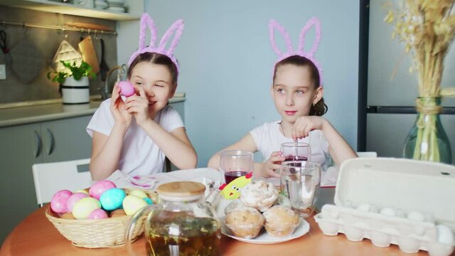 Funny little sisters wearing bunny ears painting eggs on Easter day