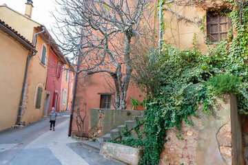 Fototapeta na wymiar Village street with orange houses and green ivy. The child walks down the street. Roussillon tourist village. Provence. France.