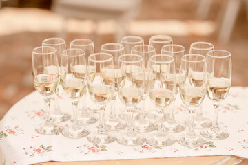 Champagne flutes half full with a bubbly fizzy alcoholic drink set on a large trey, sparkling wine in long glasses prepared for the wedding guests reception or welcoming participants at a formal event