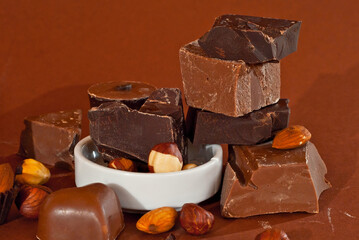 Chocolate on a pile close up. Different types of chocolate on a brown background. Nuts are poured near the chocolate.
