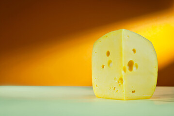 Yellow piece of cheese on an orange background. Triangular cheese close up. Copy space and free space for text near the cheese.