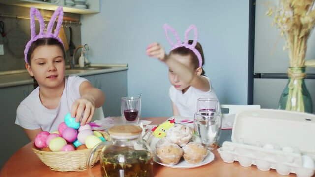 Funny little sisters put colored eggs in basket on Easter day