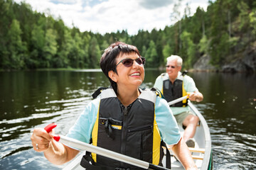 Happy mature couple in life vests canoeing in forest lake. Sunny summer day. Tourists traveling in Finland, having adventure. 