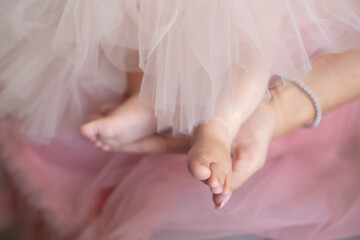 Woman wearing pink tulle dress holding delicately baby girl's bare feet wearing matching outfit,...